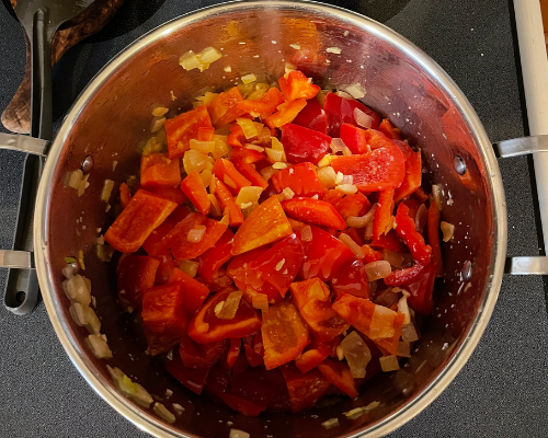 Peppers, garlic, salt and pepper all added to a pot on the stove 